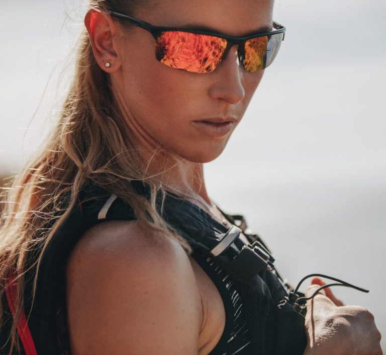 Femme avec lunettes de soleil, regard déterminé, portant un équipement de sport.