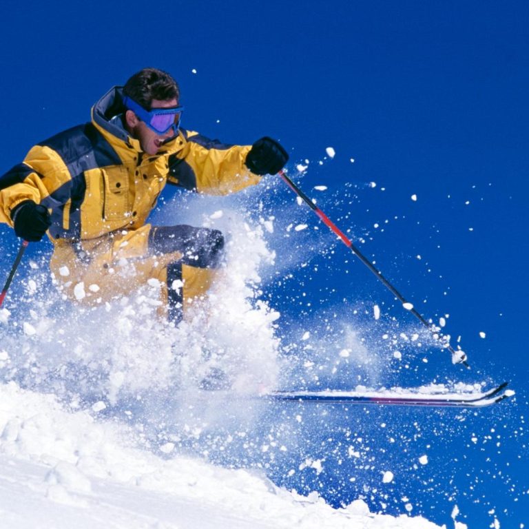 Skieur en tenue jaune effectuant un saut dans la neige sous un ciel bleu.